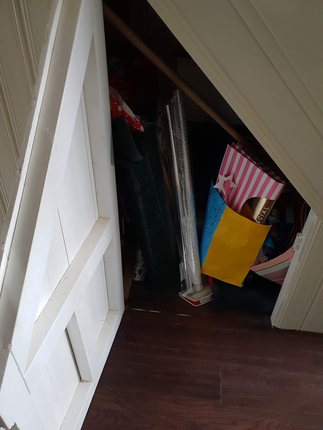 The old hinged understairs cupboard door, with bags and wrapping paper piled inside