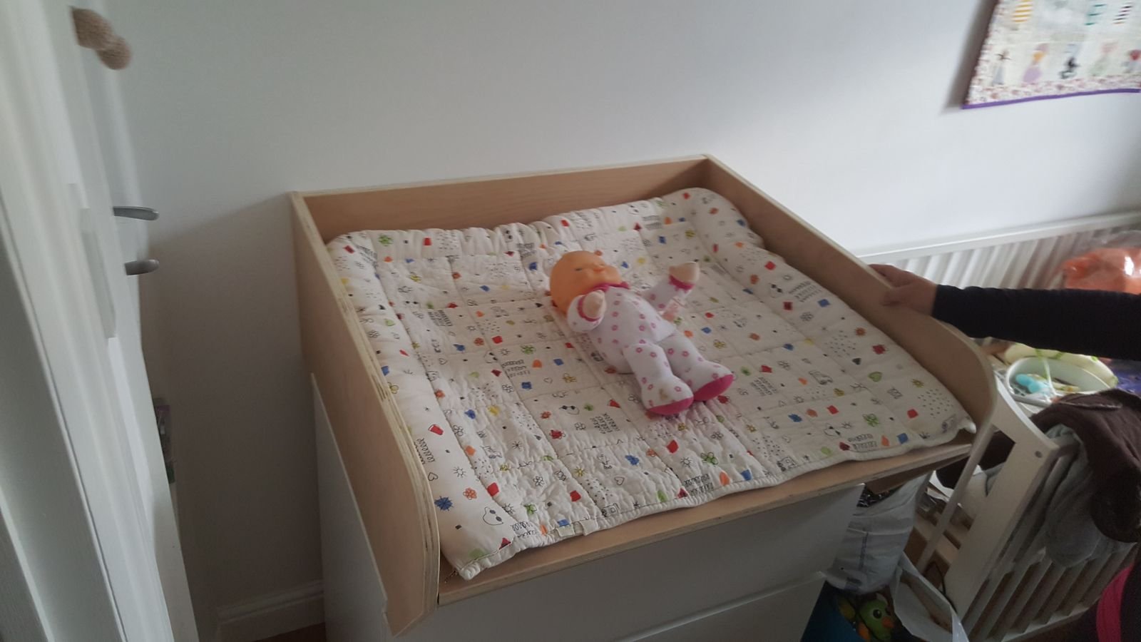 A doll lying on a changing mat in the new plywood top, sitting on a white chest of drawers