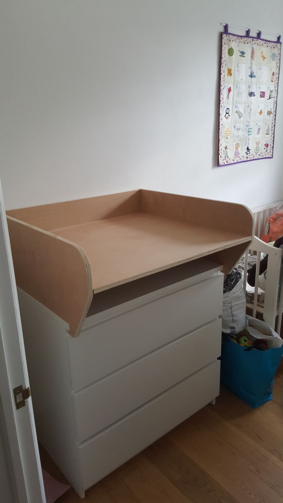 Plywood changing top with high sides sitting on a white IKEA chest of drawers